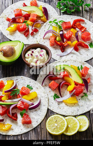 Délicieux fajitas sain avec des morceaux de saumon fumé, tranches d'avocat, le poivron, l'oignon, le persil avec de la crème en petite cuvette d'argile sur vieux dark woo Banque D'Images