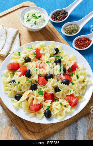 De délicieuses pâtes italiennes Farfalle au saumon fumé, olives noires parsemées de persil sur plaque blanche sur la planche à hacher, sauce crème et épices Banque D'Images