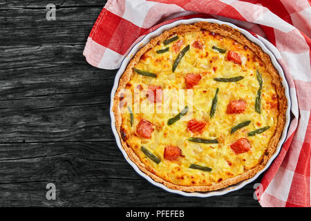 Quiche au saumon tarte délicieux,haricot vert et l'Emmental, la crème, l'oignon et les œufs dans le plat de cuisson avec l'essuie-tout sur de vieilles planches en bois foncé, v Banque D'Images