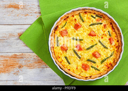 Quiche au saumon et haricots verts Tarte fine à l'Emmental, la crème, l'oignon et les œufs dans le plat de cuisson sur le tableau vert mat sur la vieille table en bois, vue du dessus Banque D'Images