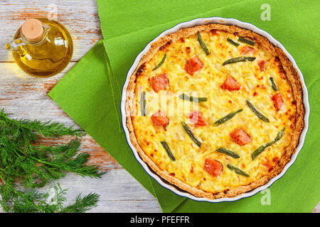 Quiche au saumon et haricots verts Tarte fine à l'Emmental, la crème, l'oignon et les œufs dans le plat de cuisson sur la vieille table en bois avec de l'aneth frais et une bouteille d'huile d'huile Banque D'Images