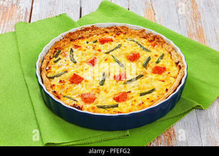 Tarte quiche délicieux saumon farci aux haricots verts,et l'Emmental, la crème, l'oignon et les œufs dans le plat de cuisson sur le vert tapis de table en bois blanc sur la vieille Banque D'Images