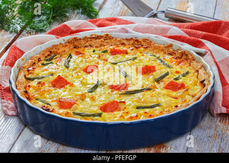 Quiche au saumon tarte, haricot vert et l'Emmental, la crème, l'oignon et les œufs dans le plat de cuisson avec cuisine serviette sur old wooden planks. aneth et spatul Banque D'Images