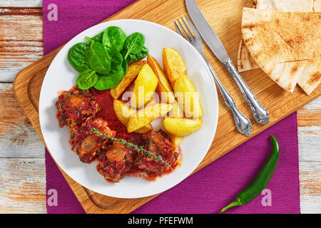 Rabo de Toro ou ragoût de bœuf servi avec salade et frites de pomme de terre sur la plaque blanche sur planche à découper avec la fourchette, le couteau et le pain pita pepp jalapeno. Banque D'Images