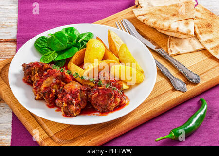 Rabo de Toro ou ragoût de bœuf servi avec salade et frites de pomme de terre sur la plaque blanche sur planche à découper avec la fourchette, le couteau et le pain pita pepp jalapeno. Banque D'Images