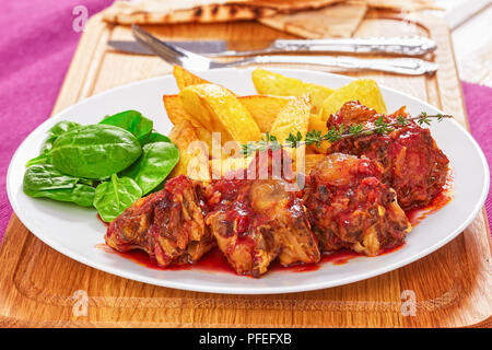 Compotée de queue de boeuf au vin rouge servi avec salade et frites de pomme de terre sur la plaque blanche sur planche à découper avec la fourchette, le couteau et le pain pita piment jalapeno. Banque D'Images