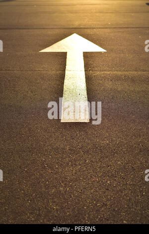 Flèche blanche peinte sur la surface scellée en jaune lumineux de la lumière du soleil du soir. Banque D'Images