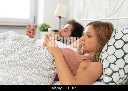 Jeune couple avec les smartphones dans leur lit. Mauvaise relation concept Banque D'Images