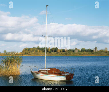 La Pologne, petit bateau, amarré, avec des moulins de la en plein air de Skansen bordant la rive du lac Lednicki en arrière-plan. Banque D'Images