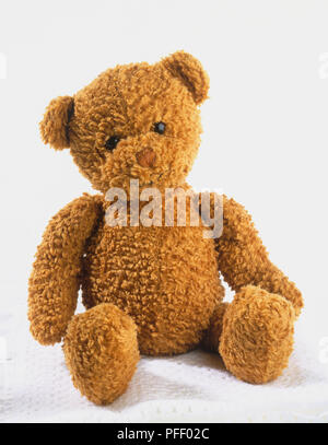 Ours en peluche brun assis sur le dessus de la couverture blanche pliée Banque D'Images