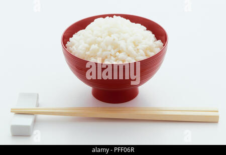Bol rouge de riz blanc ordinaire et paire de baguettes en face Banque D'Images