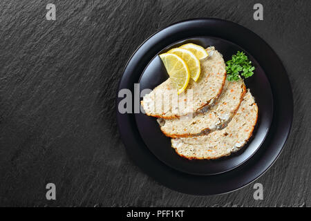 Carpe juive ou haché-poisson farci la farcissure prг©parent à l'intérieur de la peau de poisson, coupés en tranches et servi sur la plaque noire avec les tranches de citron sur le plateau en ardoise, vue à partir de Banque D'Images