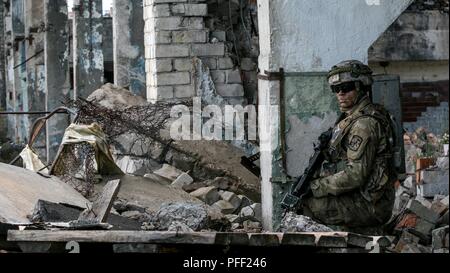 Des cadets de l'armée américain Kenneth basse, affectés à des cadets de l'armée américaine Commande, prend une position défensive offensive militaire au cours de l'entraînement en milieu urbain (MOUT) comme une partie de la grève en sabre 18 de Skrunda, Lettonie, 12 juin, 2018. Grève de sabre est un exercice multinational de 19 pays participants à l'essai sur leur capacité à travailler ensemble pour promouvoir la stabilité dans la région et d'améliorer les unités de chaque capacité d'accomplir leurs missions. désignés Banque D'Images