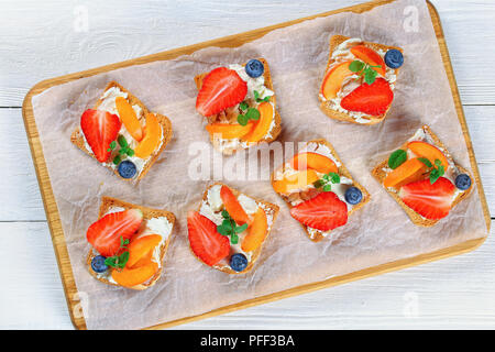 Délicieux toasts croustillant fraise abricot myrtille avec fromage à la crème tendre décoré de feuilles de menthe, sur papier sur planche de bois, vue du dessus Banque D'Images