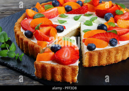Close-up of Delicious vinaigrette crémeuse au fromage gâteau décoré avec des fraises mûres, abricots, myrtilles et les feuilles de menthe avec découper une tranche sur l'ardoise Banque D'Images