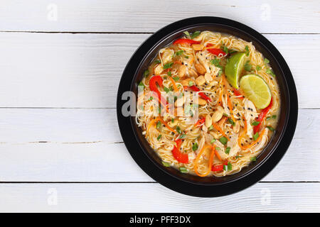 Pâte de curry vert de poulet thaï au lait de coco, légumes et fines herbes dans un bol noir parsemé de graines de sésame et d'arachide sur travail en bois Banque D'Images