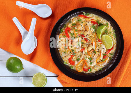 Pâte de curry vert de poulet thaï au lait de coco, légumes et fines herbes dans un bol noir parsemé de graines de sésame et d'arachide sur travail en bois Banque D'Images