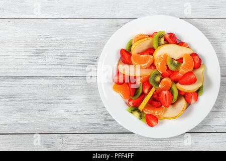 Délicieuse salade de fruits de fraises, kiwis et de tranches de poire et de mandarine sur blanc plat sur le plan de cuisine en bois, vue du dessus Banque D'Images