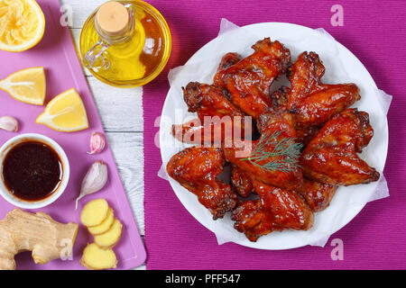 Croustillant délicieux rôtis au four miel collant des ailes de poulet au gingembre sur plaque, sur une table en bois, la sauce barbecue et ingrédients pour la marinade sur planche à découper Banque D'Images