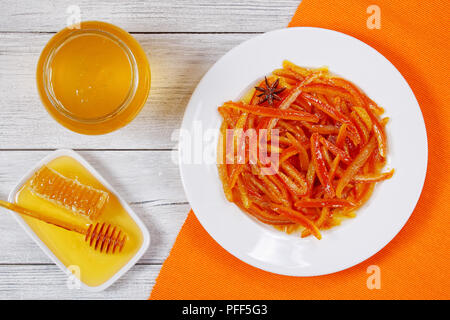 Délicieux confits Maison pelures d'orange et de citron cuit sur plaque blanche sur table en bois avec du miel, miel et la moitié d'orange sur l'arrière-plan, Banque D'Images