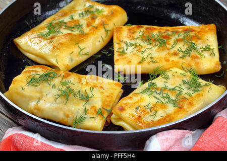 De délicieuses crêpes farcies à la mozzarella roulés sur poêlon aspergé avec de l'aneth, sur planche de bois sombre, vue de dessus, close-up Banque D'Images