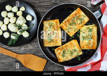 Délicieux épinards mozzarella crêpes farcies d'enrubannage sur poêlon aspergé avec de l'aneth, sur planche de bois foncé avec mini boules de mozzarella sur bl Banque D'Images