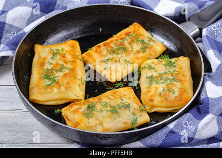 Close-up de délicieuses crêpes farcies à la mozzarella roulés sur poêlon aspergé avec de l'aneth, sur table en bois avec des serviettes de cuisine, vue d'abo Banque D'Images