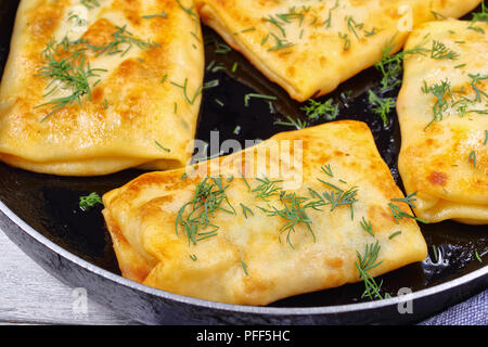 Close-up de délicieuses crêpes farcies au jambon et mozzarella wraps sur poêlon aspergé avec de l'aneth, sur table en bois avec des serviettes de cuisine, vue Banque D'Images