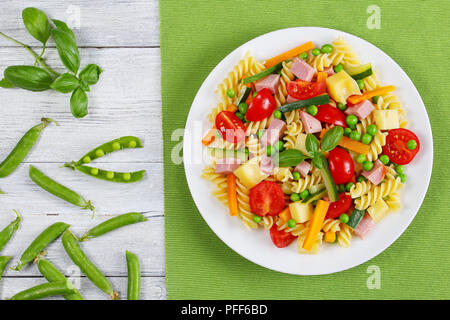 La lumière délicieuse salade de fusilli pâtes italiennes à la carotte et bâtonnets de courgette, jambon, fromage en morceaux, les pois verts, les tomates cerise sur plaque blanche sur gree Banque D'Images