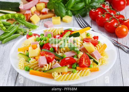 La lumière colorée sain salade de fusilli pâtes italiennes à la carotte et bâtonnets de courgette, jambon, fromage, petits pois, tomates cerises sur plaque blanche avec fo Banque D'Images