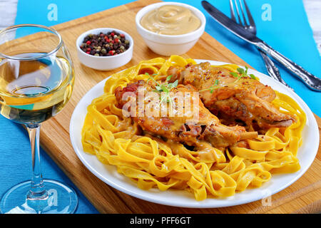 Délicieux lapin braisé ou lapin a la moutarde servi avec des pâtes sur la plaque blanche sur planche de bois avec un verre de vin blanc, recette authentique, vue arrière Banque D'Images