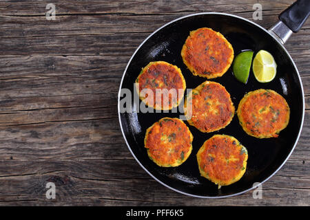 Frit délicieux cakes faits maison avec de la purée de pomme de terre sur la poêle avec les tranches de lime, sur table en bois foncé, recette classique, vue d'en haut Banque D'Images