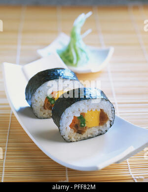 Deux parcelles de sushis dans une courbe plate, sur les petites parcelles de légumes vert flou plaque en arrière-plan, Vue de face. Banque D'Images