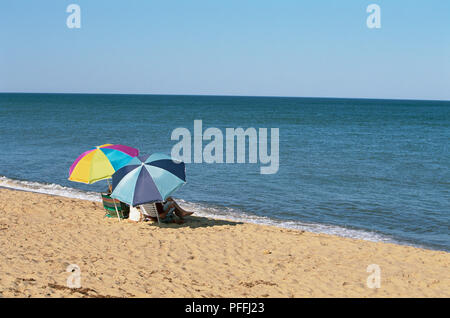 USA, Rhode Island, Misquamicut State Beach, vue arrière de deux personnes assises à l'ombre des parasols donnant sur la mer. Banque D'Images