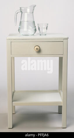 Table de chevet en bois peint, avec verseuse en verre d'eau et verre de l'eau debout sur elle. Banque D'Images