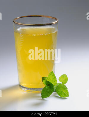 Thé à la menthe marocain dans un verre, avec une feuille de menthe à côté Banque D'Images
