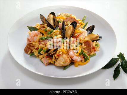 La Paella contenant les moules, crevettes, chorizo, viande et légumes, servi sur un plateau, avec le laurier par le côté Banque D'Images