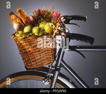 Panier en osier contenant des pommes, du pain et des fleurs, monté sur une bicyclette de guidon Banque D'Images