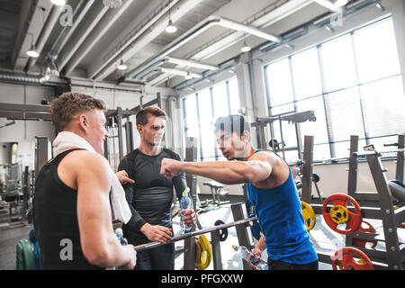 Jeunes amis debout et parler dans une salle de sport moderne, crossfit holding les bouteilles en plastique et de donner fist bump. Banque D'Images