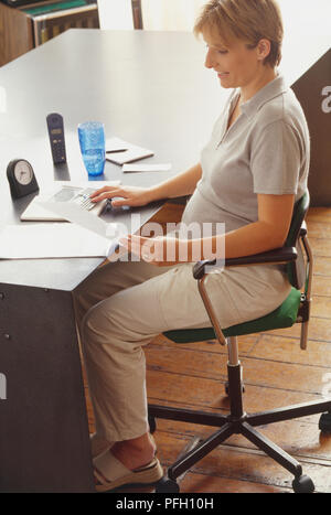Pregnant woman pointing at 24, dans un bureau. Banque D'Images
