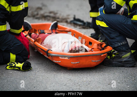 Les pompiers méconnaissables mettre une jeune femme blessée dans une civière en plastique sur la route après un accident de voiture. Close up. Banque D'Images