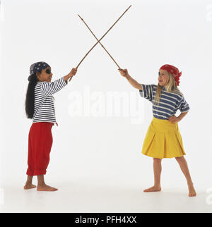 Deux jeunes filles en costumes pirate crossing twig 'swords', side view Banque D'Images