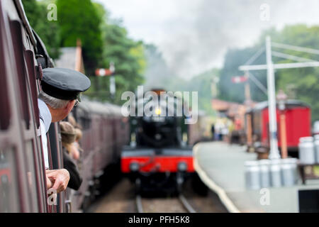 Vue arrière du contrôleur (prises en pension) vintage de transport en tant que station de train s'approche. Deuxième machine à vapeur s'approche Banque D'Images