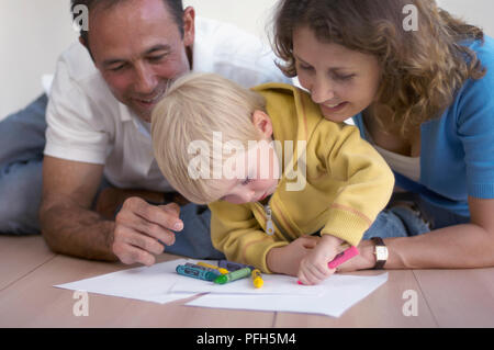 Boy peinture avec des crayons, homme et femme regardant par-dessus son épaule, regardant Banque D'Images