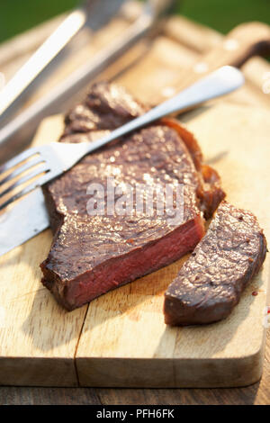 Rare-steak grillé sur planche, une tranche découpée, couverts Banque D'Images