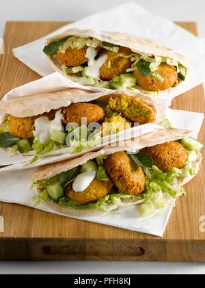 Trois sandwichs falafel farci, avec des morceaux de concombres, laitue, feuilles de menthe et sauce yogourt, avec des serviettes blanches sur planche en bois, close-up Banque D'Images