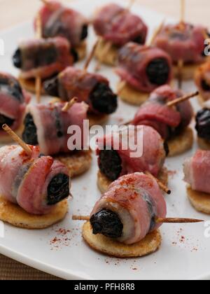 Diables à cheval, les pruneaux farcis au chutney de mangues et enrobé de bacon, saupoudrée de poivre de cayenne, disposés sur des tranches de pain grillé, close-up Banque D'Images