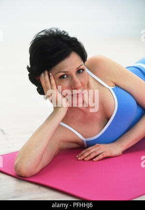 Femme couchée sur un tapis d'exercice, tête posée sur la main Banque D'Images