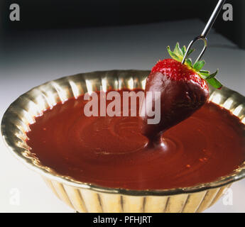 Strawberry sur fourche étant plongé dans une sauce au chocolat dans le bol en métal, Close up. Banque D'Images