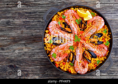 De délicieux fruits de mer paella de Valence avec des langoustines, des moules sur salé riz safrané aux épices et des tranches de citron dans la casserole, sur table en bois traditionnel, s Banque D'Images